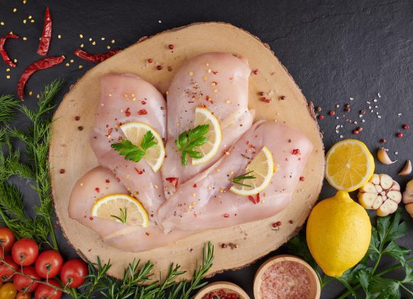 raw chicken fillet with garlic, pepper and rosemary on wooden on chopping board. fresh fillet. fresh chicken meat, chicken fillet with spices at black stone table. top view with copy space.